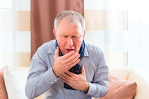 An elderly man coughing and holding his mouth